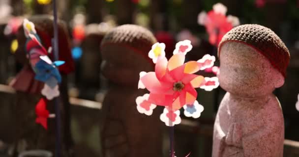 A slow motion of moving colorful windmills with Jizo statue daytime closeup — Stock Video