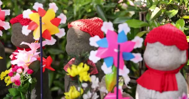 Een langzame beweging van bewegende kleurrijke windmolens met Jizo standbeeld overdag close-up — Stockvideo