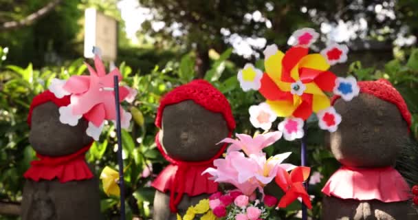 A slow motion of moving colorful windmills with Jizo statue daytime closeup — Stock Video