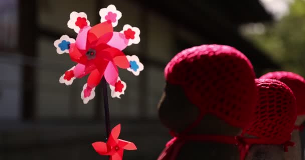 Um movimento lento de moinhos de vento coloridos em movimento com estátua de Jizo closeup diurno — Vídeo de Stock