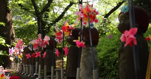 Un rallentatore di mulini a vento colorati in movimento con statua Jizo di giorno — Video Stock