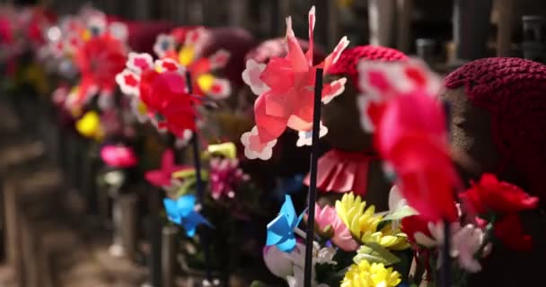 Un lent mouvement de moulins à vent colorés en mouvement avec statue Jizo en gros plan de jour — Video