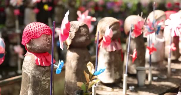 Een langzame beweging van bewegende kleurrijke windmolens met Jizo standbeeld overdag close-up — Stockvideo