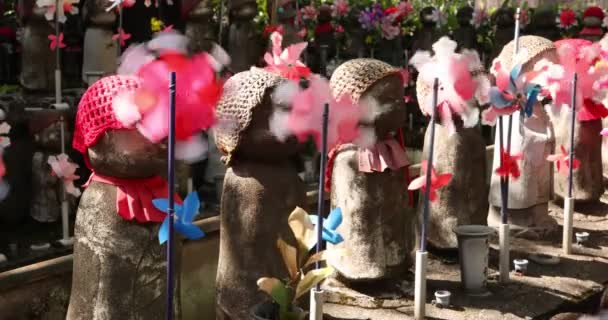 Un lent mouvement de moulins à vent colorés en mouvement avec statue Jizo de jour — Video