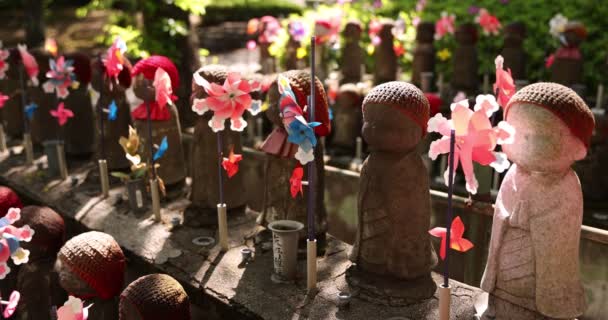 Una cámara lenta de molinos de viento coloridos en movimiento con la estatua de Jizo durante el día — Vídeo de stock