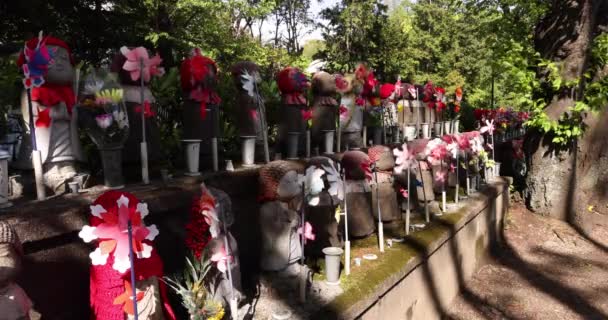 Una cámara lenta de molinos de viento coloridos en movimiento con la estatua de Jizo durante el día — Vídeo de stock