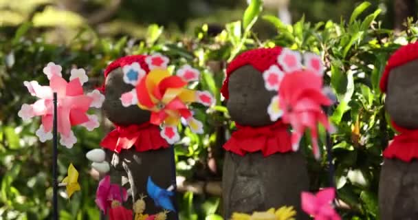 Una cámara lenta de molinos de viento de colores en movimiento con la estatua de Jizo primer plano diurno — Vídeos de Stock