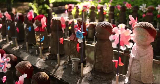 Μια αργή κίνηση των πολύχρωμων ανεμόμυλων με Jizo άγαλμα ημέρα — Αρχείο Βίντεο
