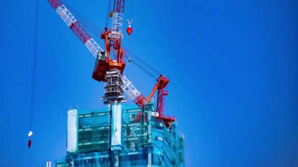 Un lapso de tiempo de la grúa de ida y vuelta detrás del cielo azul en la construcción en Tokio panorámica — Vídeos de Stock