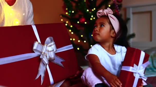 Африканский счастливый ребенок чувствует себя счастливым, чтобы получить подарки, открывая коробку с матерью и отцом, сидя на кровати дома — стоковое видео