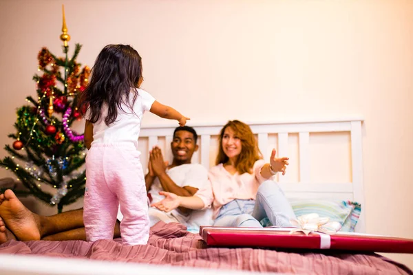 Familia mestiza despertar en dormitorio feliz niña bailando y saltando en la cama — Foto de Stock