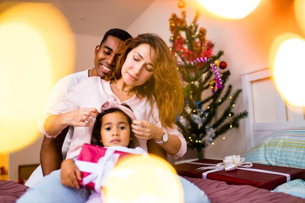 Mezcla de raza feliz familia sentado en la cama y dando una gran caja roja regalo de Navidad en la víspera de la mañana — Foto de Stock