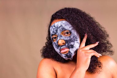 Kahverengi arka planda, yüzünde baloncuk maskesi olan genç bir kadın.