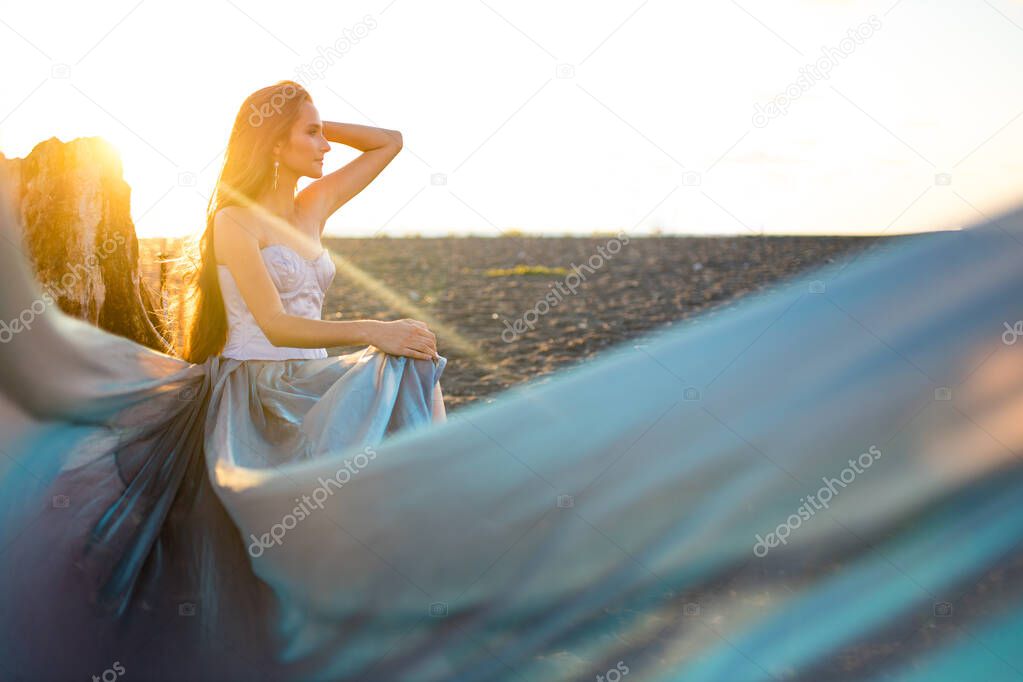 Beautiful long haired woman dressed a mermaid sitting on the sand beach background