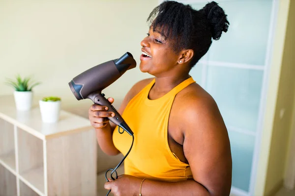 Όμορφη αφρο γυναίκα στεγνώνοντας τρίχες και τραγουδώντας σαν μικρόφωνο — Φωτογραφία Αρχείου