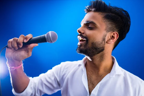 indian man in white shirt with beard singing in recording studio on blue background