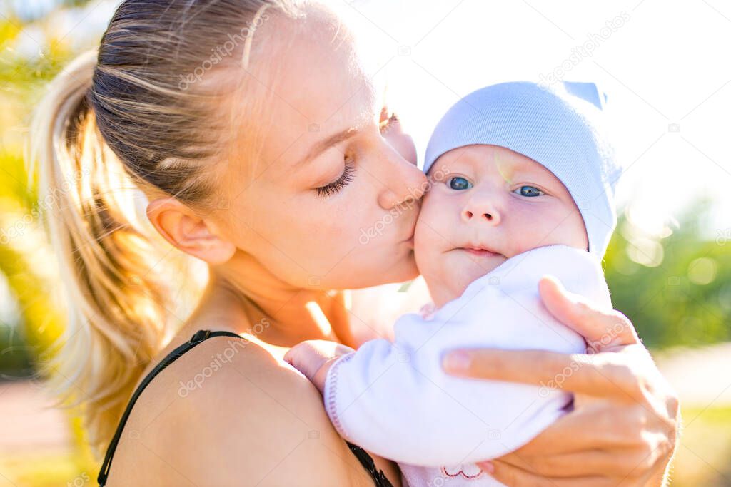 happy blonde woman kissind and feelinf adore to her stroll new born kid in tropics beach park outdoors