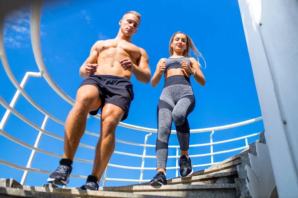 Jovem casal em roupas esportivas fazendo exercícios matinais ao ar livre em escadas quentes de verão — Fotografia de Stock