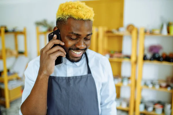 Afro mužský hrnčíř mluví do telefonu ve svém studiu — Stock fotografie