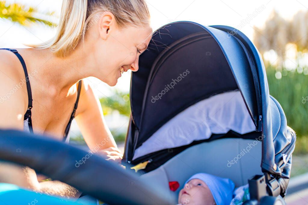 happy blonde woman kissind and feelinf adore to her stroll new born kid in tropics beach park outdoors