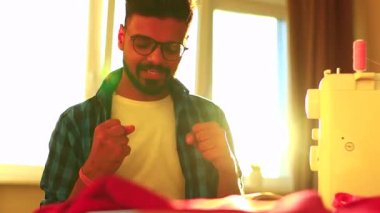 Hintli yakışıklı sakallı adam masada oturmuş dikiş aletleri dikip dans ediyor.