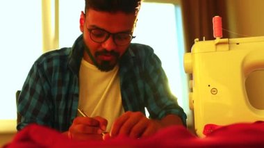 Hintli yakışıklı sakallı adam masada oturmuş dikiş aletleri dikip dans ediyor.