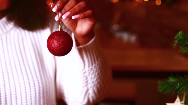 Femme hispanique américaine mettre la boule rouge clignotant sur la branche dans le salon le soir — Video