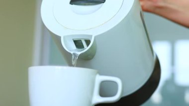 Kadın, çay demlerken bardağa kaynar su döküyor.