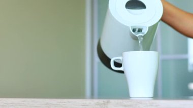 Kadın, çay demlerken bardağa kaynar su döküyor.