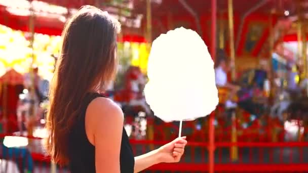 Smutna młoda kobieta jedząca watę cukrową - karuzela w parku rozrywki w tle — Wideo stockowe
