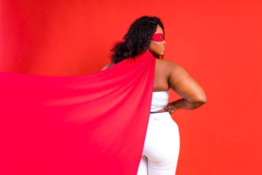 Kırmızı gözlü Latin kadın ve stüdyo arka planında uzun süper kahraman pelerini.