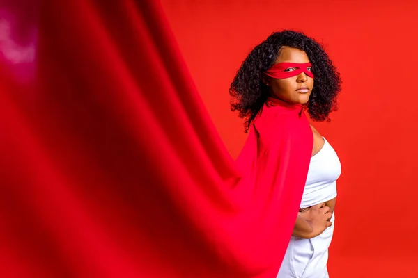 Donna ispanica latina in maschera occhi rossi e lungo mantello da supereroe sullo sfondo dello studio — Foto Stock