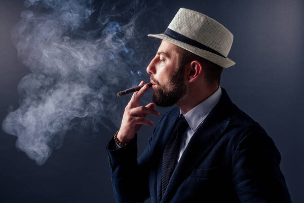 Портрет привлекательного бизнесмена с сигарой на черном фоне студии