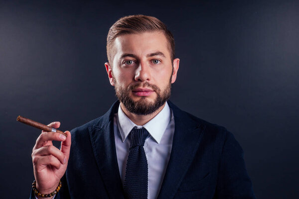 Портрет привлекательного бизнесмена с сигарой на черном фоне студии