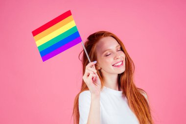 Beyaz tişörtlü kızıl saçlı kadın stüdyoda gökkuşağı bayrağı taşıyor.