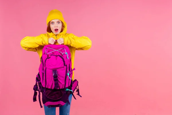 Szczęśliwa kobieta gotowa do wędrówki w nieznanym miejscu nosi duży plecak na ramionach w różowym tle studio — Zdjęcie stockowe