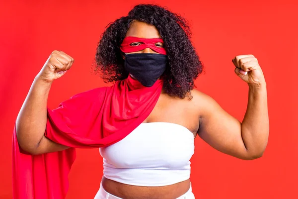 Lateinisch hispanische Frau mit roter Augenmaske und langem Superheldenmantel im Studiohintergrund — Stockfoto