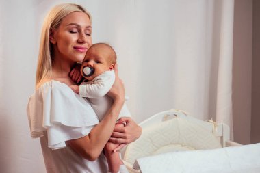 Sarışın anne rahat bir dairede bebeği emzirip kucaklıyor.