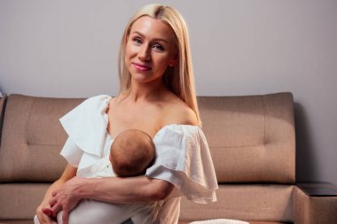 Sarışın anne rahat bir dairede bebeği emzirip kucaklıyor.