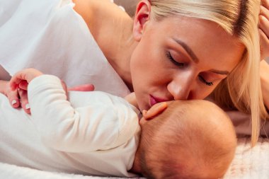 Yeni doğmuş bebek. Annesinin şefkatle kucağında. Yatak odasında, yatağa uzanmış.