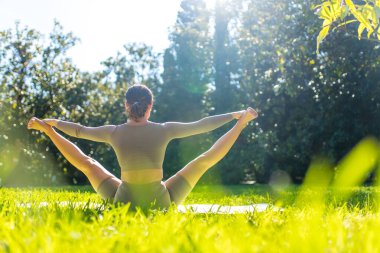 Parkta akrobatik yoga yapan, yaz sabahı tek başına egzersiz yapan esnek bir kadın.