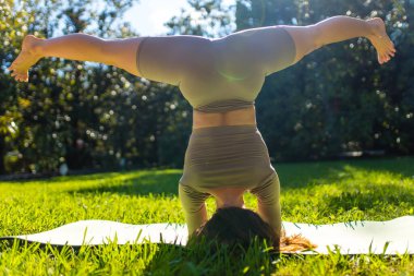 Parkta akrobatik yoga yapan, yaz sabahı tek başına egzersiz yapan esnek bir kadın.