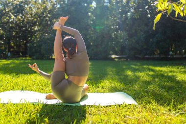 Parkta akrobatik yoga yapan, yaz sabahı tek başına egzersiz yapan esnek bir kadın.