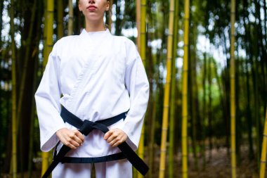 Siyah kuşaklı genç bir kadın dövüş sanatları koçu bambu arka planda.