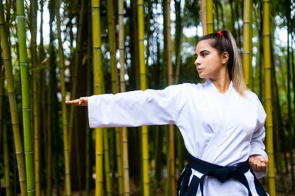 Een jonge vrouw met een zwarte riem coaches in krijgskunst outdoor bamboe achtergrond — Stockfoto