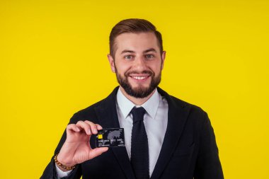 Sarı arka planda kredi kartı tutan yakışıklı genç iş adamının portresi.