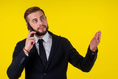 Telefonda konuşan genç yakışıklı bir adamın portresi, sarı arka planda izole edilmiş akıllı telefonu kulağının yanında tutuyor.