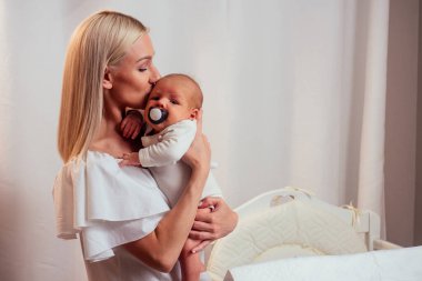 Sarışın anne rahat bir dairede bebeği emzirip kucaklıyor.