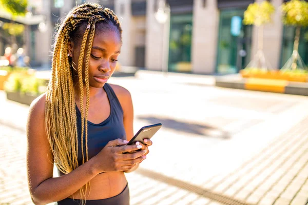 Afrika amerikansk flicka med långa gula dreadlocks flätor använder tränare träna app utomhus i centrum väntar taxi — Stockfoto