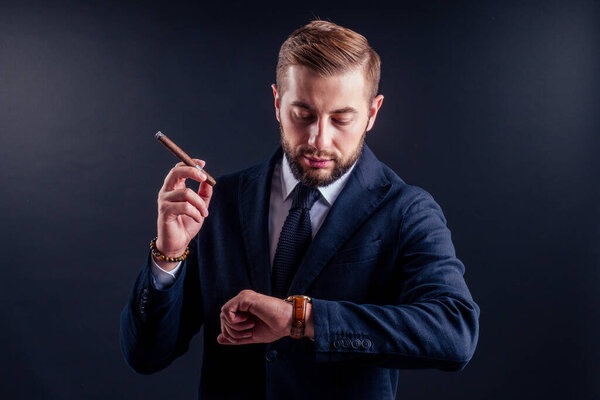 Портрет привлекательного бизнесмена с сигарой на черном фоне студии